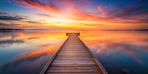Naklejka premium A Wooden Dock Leading Out To a Calm Lake With a Vibrant Sunset Reflecting In The Water