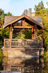 A wooden gazebo with a slanted roof sits in front of a building