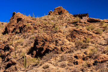 A rocky hillside with a few cacti and a small building in the distance