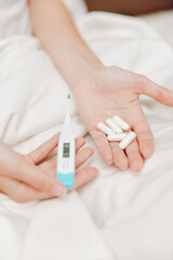 Sick person in bed holding thermometer with pills on bedside table