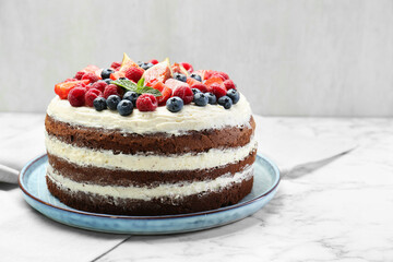 Delicious chocolate sponge cake with berries on white marble table