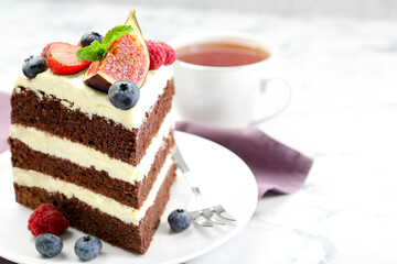Piece of delicious chocolate sponge cake with berries and tea on white table, closeup