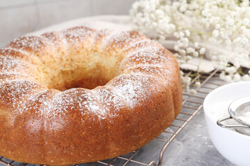 Freshly baked sponge cake with powdered sugar and flowers on grey table, closeup
