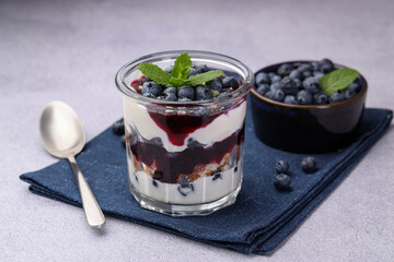 Tasty trifle dessert. Blueberries, sponge cake and whipped cream in glass on light grey table