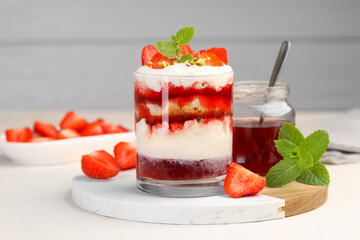 Tasty trifle dessert. Strawberries, sponge cake and whipped cream in glass on beige table