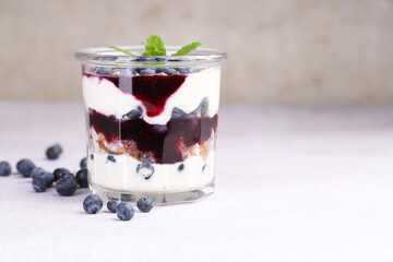 Tasty trifle dessert. Blueberries, sponge cake and whipped cream in glass on light grey table, space for text