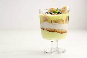 Tasty trifle dessert. Banana, blueberries, sponge cake and whipped cream in glass on white wooden table, space for text