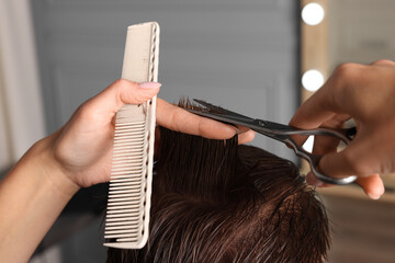Naklejka premium Professional hairdresser cutting client's hair with scissors in barbershop, closeup