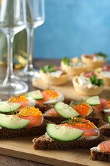 Tasty canapes with salmon and cucumber on wooden table, closeup