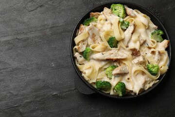 Delicious pasta Alfredo with chicken, cheese, creamy sauce and broccoli on black table, top view. Space for text
