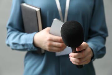 Journalist with microphone, smartphone and notebook on grey background, closeup