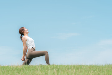 青空の下でヨガ・ピラティス・ストレッチをする若いアジア人女性
