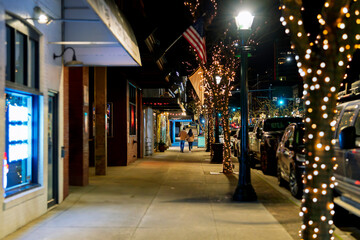Late night view as pedestrians walk along the illuminated main street of downtown Coeur d'Alene, Idaho, with illuminated trees at Christmas time. © Kirk Fisher