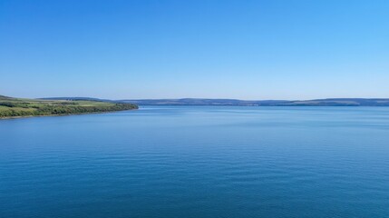 Serene Blue Water Under Clear Sky with Lush Green Hills in Background