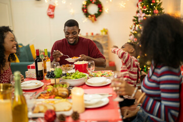 A warm Christmas family dinner with a father serving food to his young child, surrounded by festive decorations, a Christmas tree, and a holiday table spread. Joyful and cozy holiday atmosphere.