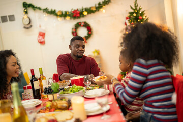 A warm Christmas family dinner with a father serving food to his young child, surrounded by festive decorations, a Christmas tree, and a holiday table spread. Joyful and cozy holiday atmosphere.