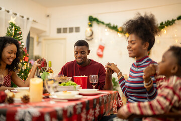 A warm Christmas family dinner with a father serving food to his young child, surrounded by festive decorations, a Christmas tree, and a holiday table spread. Joyful and cozy holiday atmosphere.