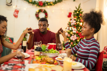 A family enjoys a festive Christmas dinner, sharing food and creating memories. A beautifully decorated Christmas tree and wreath add warmth, while candles and decor enhance the cozy holiday setting.