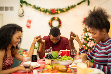 A family enjoys a festive Christmas dinner, sharing food and creating memories. A beautifully decorated Christmas tree and wreath add warmth, while candles and decor enhance the cozy holiday setting.