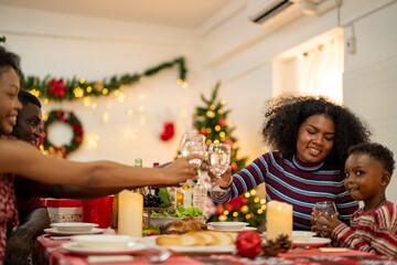 A joyful family gathers around the dinner table celebrating Christmas. The father, dressed in a Santa hat, gives a gift to the child, while everyone smiles with warmth and festive decorations.