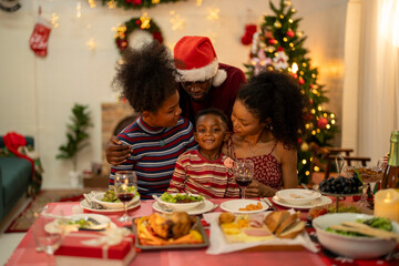 A joyful Christmas celebration with friends gathered around a festive dining table. Featuring a man in a Santa hat, a decorated Christmas tree, delicious food, and warm holiday cheer.