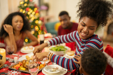 A joyful Christmas celebration with friends gathered around a festive dining table. Featuring a man in a Santa hat, a decorated Christmas tree, delicious food, and warm holiday cheer.