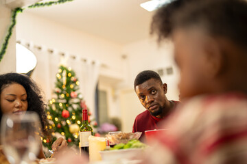 A festive family Christmas dinner setting with a decorated tree in the background. The family gathers around a beautifully decorated table, sharing food, joy, and warmth in the holiday spirit.