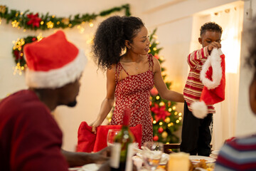 A joyful family gathering in a festive living room decorated for Christmas, featuring a Christmas tree, garlands, and fireplace, as they share warm moments and holiday cheer together