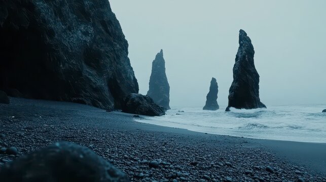Dramatic coastal scene; dark volcanic rock formations on a black sand beach meet moody ocean waves under a misty sky.
