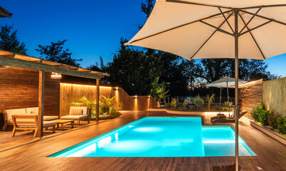 Backyard swimming pool with wooden deck and large umbrella in cozy ambiance. Luxury outdoor...