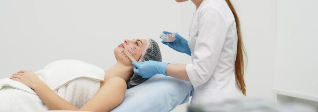 Close-up of a cosmetologist&rsquo;s hands applying an alginate mask with rose petals to a young woman&rsquo;s face in a professional beauty salon. Shot on anamorphic lens in 2.39