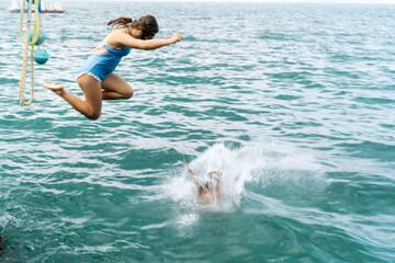 Children are filled with excitement as they leap into the clear blue sea, splashing water joyfully.