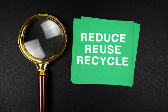 Reduce Reuse Recycle text on sticky note with magnifying glass on black background