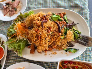 Deep fried Thai Nile Tilapia fish dressing with crispy shredded lemon grass serving on the plate. Famous local seafood menu in Thai restaurant.