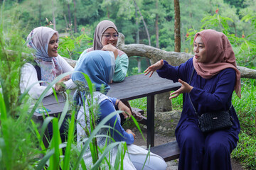 Yogyakarta, 21 December 2024. Four women wearing hijabs enjoy a lively conversation at a wooden table in a lush green outdoor setting. 