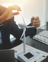 Shut of handsome business man working on new alternative energy development looking at a model of a wind turbine in modern startup.