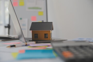 Wooden table with laptop, house keys Clipboard with pen, house model and green tree calculator, real estate concept. close up pictures