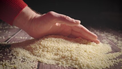 Hand gently touching raw rice grains scattered on dark wooden table in slow motion
