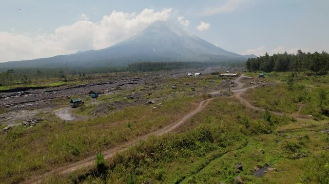 4K Drone Video flying up to view Semaru Volcano, surrounded by green forest landscapes and molton rock with cars and motorbikes driving the volcanic roads in East Java Indonesia