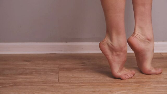 Slender female bare feet are walking against background of a blue wall at home. Attractive legs woman graceful walk on tiptoes in apartment. Foot and body care, posture concept. Closeup