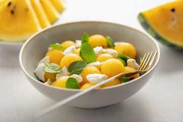 Summer fresh salad with yellow watermelon, ricotta, and mint leaves in  bowl on the table.