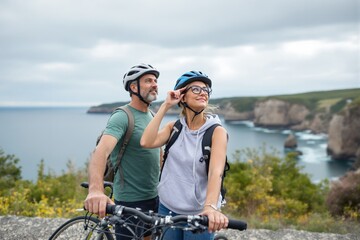 Couple enjoying a cycling adventure near a coastal cliff on a cloudy day.