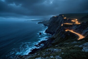 Coastal cliff road with illuminated curves by night under dramatic cloudy sky, ocean waves crashing below.