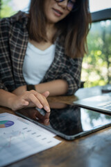 A woman is sitting at a table with a tablet and a laptop. She is using the tablet to point at something on the laptop. The scene suggests that she is working on a project or presentation