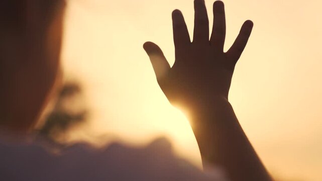 silhouette of hand of girl child in sun glare. faith in god religion concept. close up hand child girl fingers silhouette at sunset sun glare in nature. dreams religion future concept lifestyle