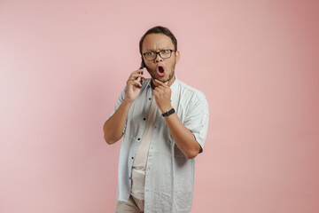 Shocked young Asian man holding his chin while using smartphone to have a call.