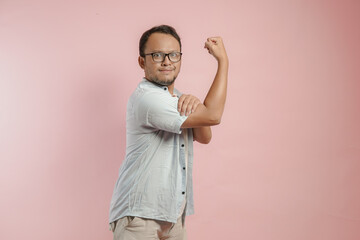 Excited Asian man showing strong gesture by lifting his arms and muscles smiling proudly.