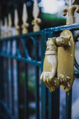 A detailed close-up of a golden door knocker in the shape of a hand, attached to an ornate green gate.