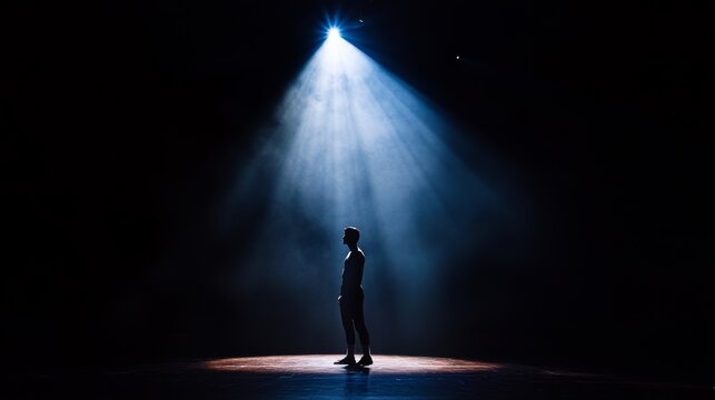 Silhouette of a person standing alone in a spotlight on a dark stage. - Powered by Adobe