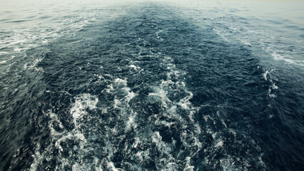 A captivating view of turbulent water in the wake of a boat, showcasing the deep blue sea and white foam patterns